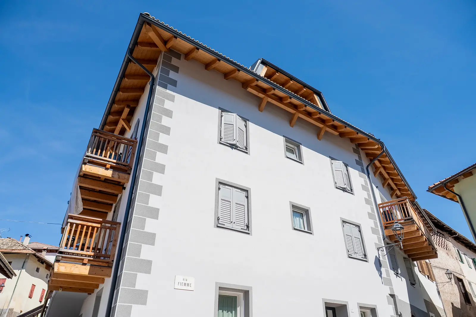 Facciata bianca a tre piano con balconi in legno e infissi grigi a Castello di Fiemme
