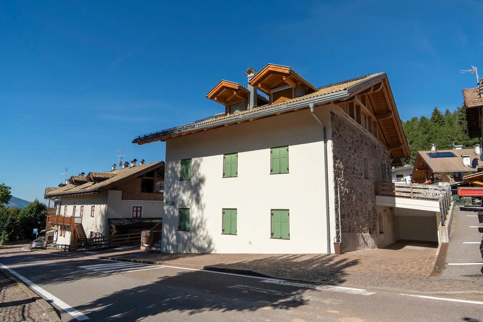 Facciata bianca di un condominio ristrutturato che dà sulla strada in via Alpini a Varena