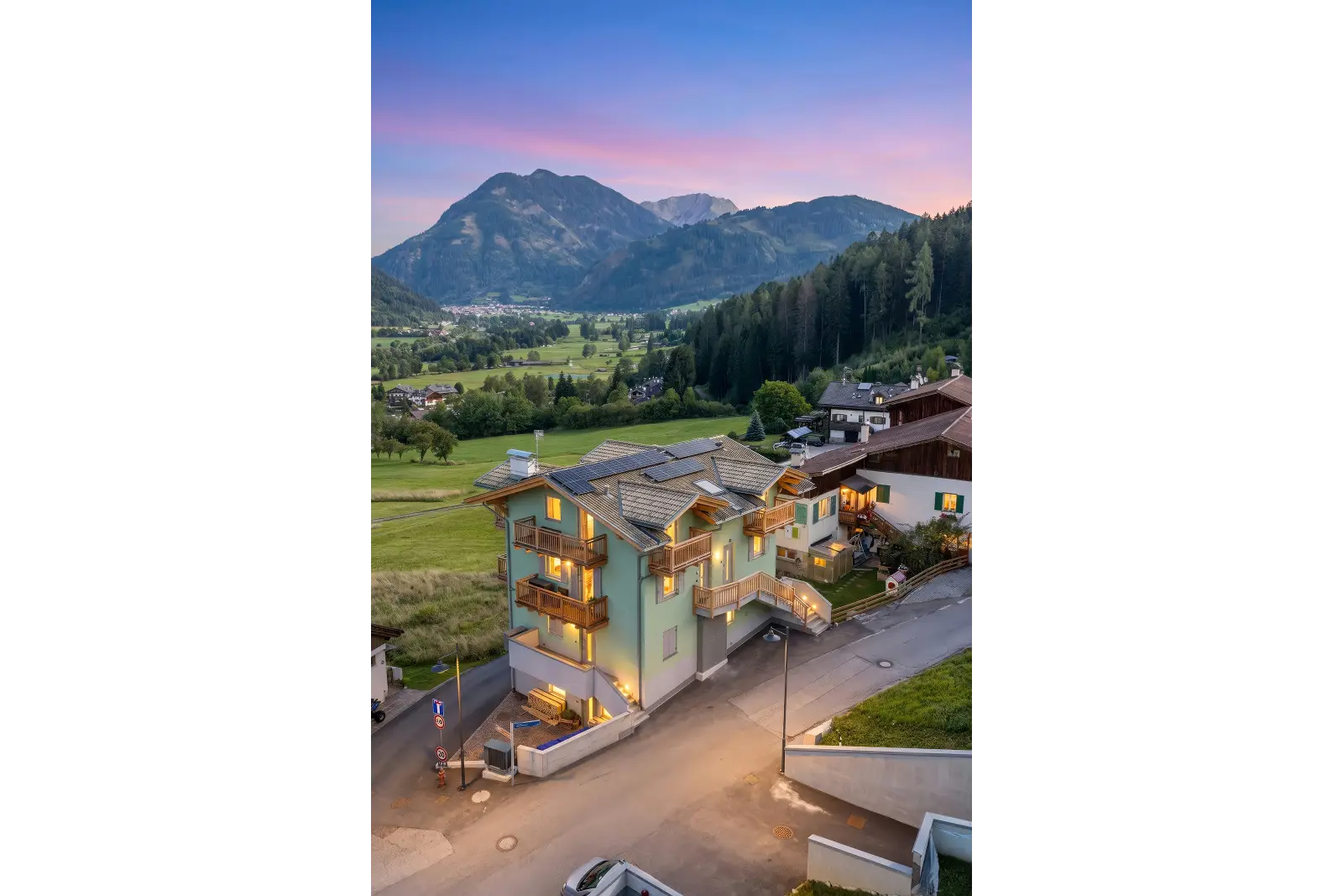 Foto da lontano di un condominio ristrutturato con le Dolomiti di sfondo a Ziano di Fiemme